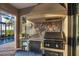 Stone encased outdoor kitchen with grill, refrigerator, tile backsplash, and lake view at 16309 Castle Park Ter, Lakewood Ranch, FL 34202