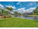 Waterfront backyard view with lush green lawn, boat dock, and tropical landscaping under a sunny, partly cloudy sky at 1038 Contento St, Sarasota, FL 34242