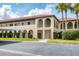 Beige two-story condominium building with arched entryways, red tile roof, trimmed bushes, and black parking lot at 3690 Pinecrest St # 114, Sarasota, FL 34232