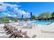 Community pool with chairs and tables for lounging on the pool deck under sunny skies with blue umbrellas at 9470 High Gate Dr # 2213, Sarasota, FL 34238