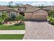 Charming front exterior with a manicured lawn, stone accents, and a brick driveway at 13587 Vancanza Dr, Venice, FL 34293