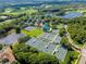 Expansive aerial view showcasing the well-maintained tennis courts surrounded by mature trees and community lakes at 7624 Boltons Ct, Bradenton, FL 34201