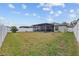 A spacious backyard with green grass, a vinyl fence, and a screened in patio with string lights at 13422 Willow Bluestar Loop, Riverview, FL 33579