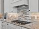 Close-up of a kitchen stovetop with granite counters, subway tile backsplash, and white cabinets at 16614 Berwick Ter, Lakewood Ranch, FL 34202