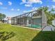 The screened in-ground pool is in the backyard with grass, a fence, trees, and a home in the background at 8304 Fishhawk Ave, New Port Richey, FL 34653