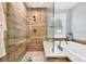 Walk-in shower featuring wood-look tile, glass enclosure, and a soaking tub with a bright shuttered window at 425 46Th Nw St, Bradenton, FL 34209