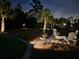 Night scene of backyard fire pit area with Adirondack chairs, lighting, and mature landscaping at 6875 Beckwith Ave, North Port, FL 34291