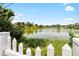 Picturesque lake view framed by a classic white picket fence and vibrant lakeside vegetation at 10827 Village Green Ave, Seminole, FL 33772