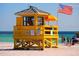 A yellow lifeguard stand on a sandy beach with clear blue waters, families and American flag visible at 111 Whispering Sands Cir # V38, Sarasota, FL 34242