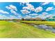 Expansive green lawn and pond with a row of houses and vibrant blue sky in the background at 12815 24Th Street E Cir, Parrish, FL 34219