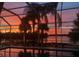 Screened-in pool reflecting a stunning orange and purple sunset, set against a backdrop of palm trees and a tranquil lake at 13167 Fernando St, Venice, FL 34293