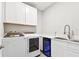 Bright laundry room featuring white cabinetry, sink, and a modern washer and dryer unit at 620 Nasturtium Ct, Nokomis, FL 34275