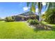 A backyard view of a screened-in lanai, lush green grass, and tropical landscaping at 6143 9Th Avenue Ne Cir, Bradenton, FL 34212