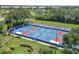 Aerial view of community tennis courts with red and blue surfaces, surrounded by mature landscaping and spectator seating at 802 Montrose Dr # 204, Venice, FL 34293