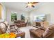 Bright living room featuring reclining leather sofas, ceiling fan, and large windows overlooking lush greenery at 13112 Swiftwater Way, Bradenton, FL 34211