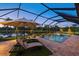 Covered pool area with lounge chairs and umbrella overlooking the lake in the backyard at 20831 Valprato Ct, Venice, FL 34293
