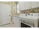 Functional laundry room featuring a side-by-side washer and dryer, white cabinetry, and tropical-themed wallpaper at 12240 Thornhill Ct, Lakewood Ranch, FL 34202