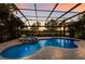 Beautiful screened-in pool area with a spa, lush landscaping, and views of the lake at sunset at 13706 American Prairie Pl, Lakewood Ranch, FL 34211