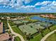 An aerial view of the community tennis courts, with a nearby lake and lush landscaping, on a beautiful sunny day at 20542 Trattoria Loop, Venice, FL 34293