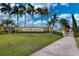 View of the Grand Paradiso community sign, with lush landscaping, a sidewalk, and palm trees under a blue sky at 20542 Trattoria Loop, Venice, FL 34293