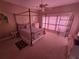 A pink bedroom with a four-poster bed, ceiling fan, and a large window at 7732 N Mobley Rd, Odessa, FL 33556
