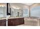 Bright bathroom featuring a double vanity with dark wood cabinets and a soaking tub next to windows at 1934 Bougainvillea St, Sarasota, FL 34239