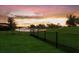 Spacious backyard featuring a black fence, overlooking a beautiful lake with fountains and a vibrant sunset at 16807 Barnwood Pl, Bradenton, FL 34211