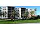 Exterior view of a bright condo building with palm trees, green grass, and ample parking at 2045 Gulf Of Mexico Dr # M1-302, Longboat Key, FL 34228