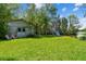 Spacious backyard with green grass, shade from lush trees, an outbuilding, and a charming fire pit near the water's edge at 3919 Fan Palm Ct, Land O Lakes, FL 34638