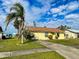 Charming single-story home with a yellow exterior, well-maintained lawn and a brown roof under a partly cloudy sky at 6113 Mckee St, Port Charlotte, FL 33981
