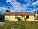 Charming single-story home with a yellow exterior, well-maintained lawn and a brown roof under a partly cloudy sky at 6113 Mckee St, Port Charlotte, FL 33981