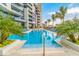 Beautiful pool featuring clear blue water, tropical foliage, and a modern building with glass balconies in the background at 1155 N Gulfstream Ave # 406, Sarasota, FL 34236