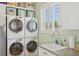 Bright laundry room with stacked washer and dryer units and a sink under a window with plantation shutters at 26 Sandy Hook S Rd, Sarasota, FL 34242