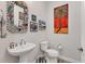 Half bath featuring an ornate mirror, floating sink, toilet, and a vibrant painting of a palm tree at 523 Wildlife Gln, Bradenton, FL 34209