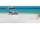 Relaxing beach view features two people on beach chairs, turquoise water, and a colorful umbrella at 6512 Midnight Pass Rd # 303, Sarasota, FL 34242