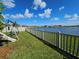 A backyard with a playset and a fence running along the lakefront under a blue sky filled with fluffy white clouds at 13156 Merlot Sunstone Cv, Parrish, FL 34219