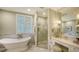 Elegant bathroom featuring a soaking tub, marble shower, and vanity area with a large mirror and shuttered windows at 420 Golden Gate Pt # 200A, Sarasota, FL 34236