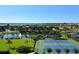 Aerial view of tennis courts surrounded by lush greenery, a pond with a fountain, and views of the water at 606 Riviera Dunes Way # 306, Palmetto, FL 34221