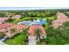 An aerial view of a house with a red tile roof, surrounded by trees and overlooking a large lake at 8118 Stirling Falls Cir, Sarasota, FL 34243