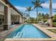 A backyard with a swimming pool, waterfall feature and chairs under palm trees on a sunny day at 8316 Portlight Ct, Lakewood Ranch, FL 34202