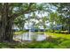 Scenic view of a pond with fountain and banyan trees behind blue and white homes at 1311 Siesta Bayside Dr # 1311-A, Sarasota, FL 34242
