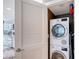 A stacked washer and dryer unit behind a white shutter door, with a glimpse of a modern kitchen nearby at 2425 Gulf Of Mexico Dr # 6A, Longboat Key, FL 34228