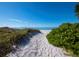 Path through dunes leads to a pristine sandy beach and tranquil blue waters under a clear sky at 3320 Gulf Of Mexico Dr # 208C, Longboat Key, FL 34228