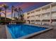 Beautiful community pool area with palm trees and multi-story condo building with a colorful sunset sky at 4200 Gulf Dr # 104, Holmes Beach, FL 34217