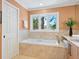Inviting bathroom showcasing a soaking tub with travertine surround, window views, and vanity with storage at 7320 Melaleuca Way, Siesta Key, FL 34242