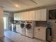 Bright laundry room features upper cabinets, modern washer and dryer, beverage cooler and tile flooring at 1204 Sunrise Rd, Venice, FL 34293