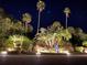 Night view of a tropical entrance adorned with palm trees, lush landscaping, and illuminated ground lighting at 4840 Gulf Of Mexico Dr # Villa 15, Longboat Key, FL 34228