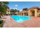 Community pool with clear blue water, brick patio, ample seating, and yellow buildings in a tropical setting at 7179 Boca Grove Pl # 202, Lakewood Ranch, FL 34202