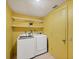 Bright laundry room in yellow featuring washer, dryer, hanging rack and floating storage shelves at 217 High Point Dr # 217A, Englewood, FL 34223