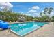 Beautiful community pool with blue water, a slide, and deck chairs, surrounded by tropical plants and clear blue sky at 4103 61St E Ave, Bradenton, FL 34203